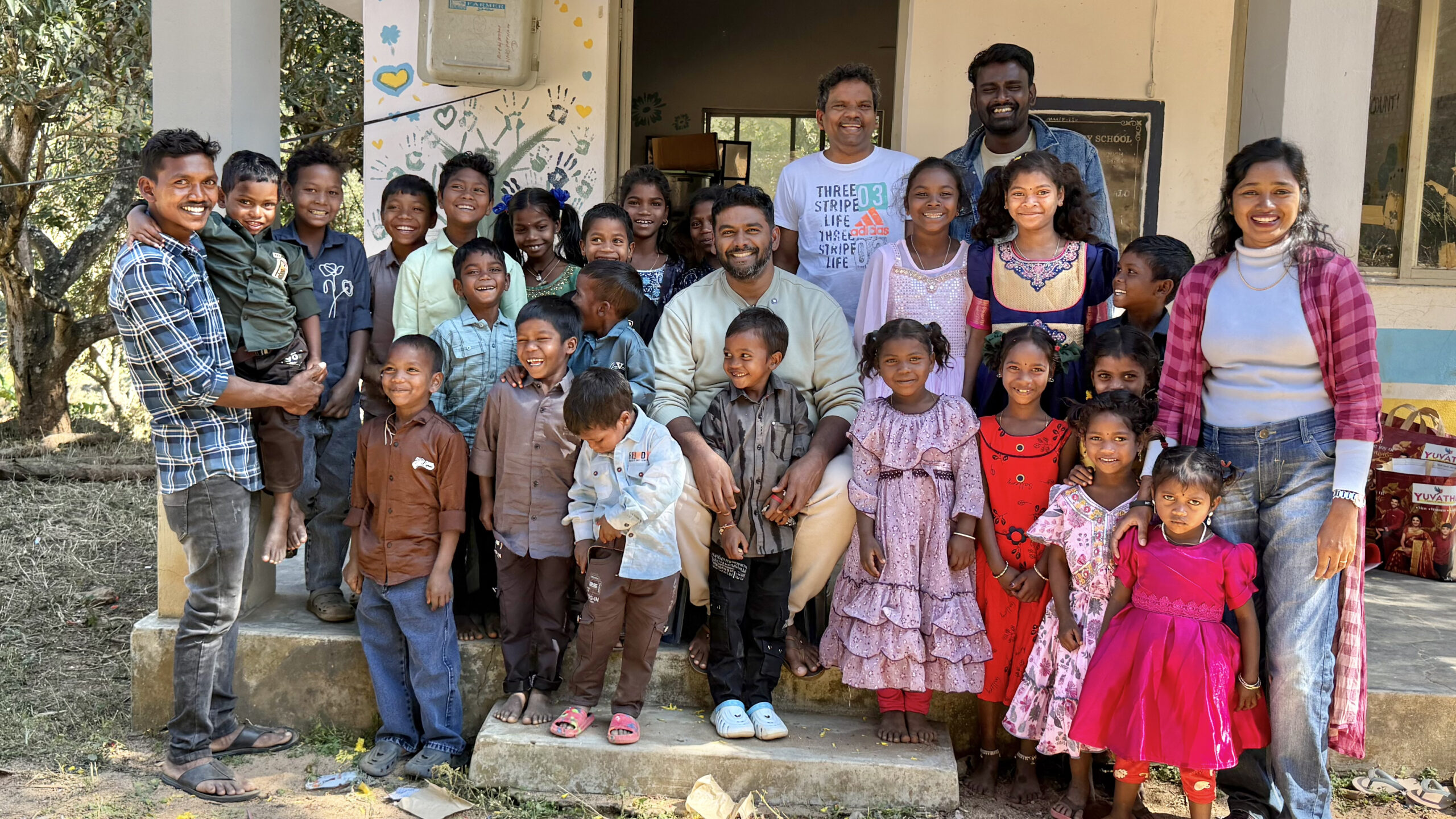 Josh Komanapalli with a group of smiling children on the steps of a village school in India